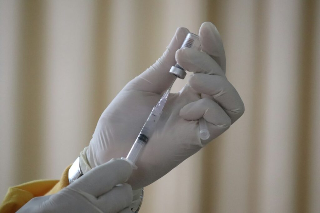 Gloved hand drawing vaccine liquid from a vial into a syringe