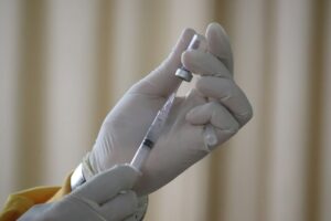 Gloved hand drawing vaccine liquid from a vial into a syringe
