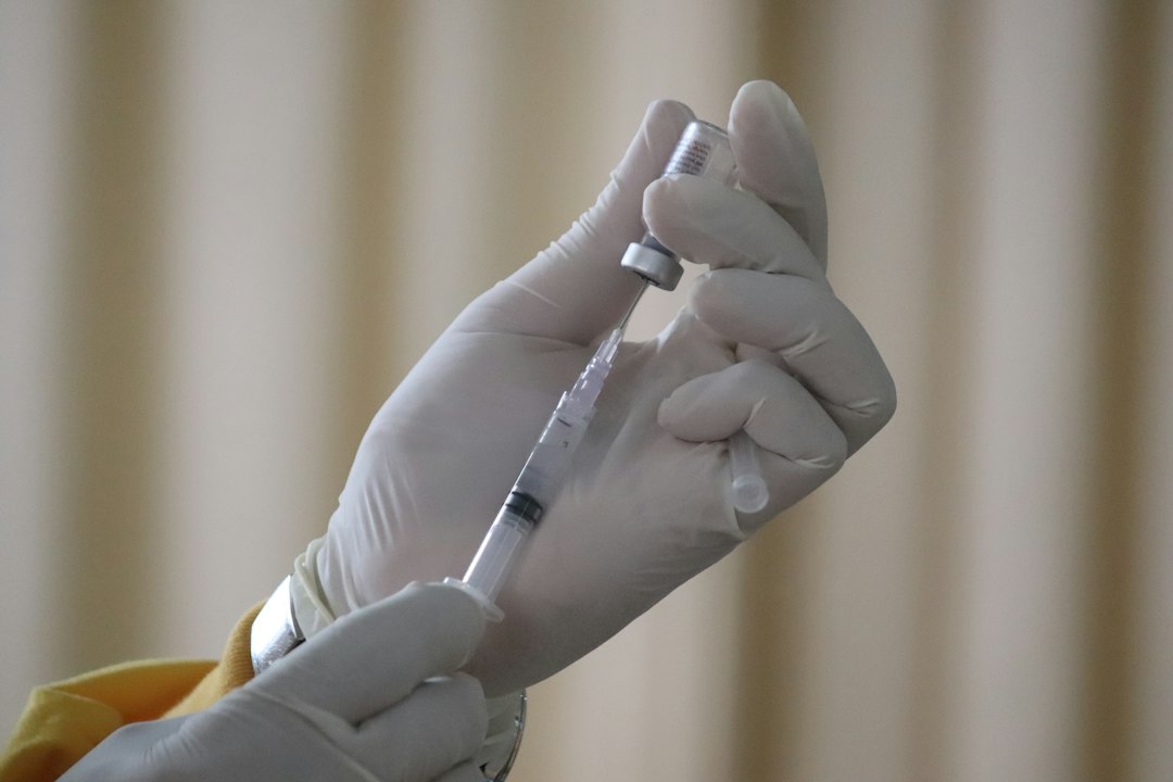 Gloved hand drawing vaccine liquid from a vial into a syringe