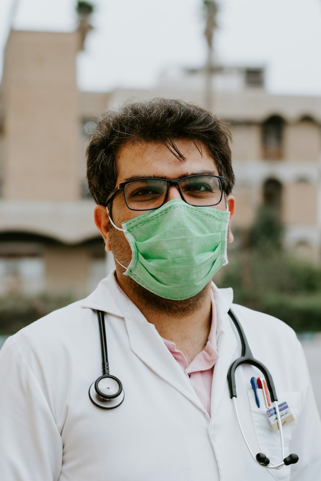 Healthcare worker in a white scrub suit wearing a green face mask